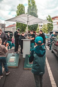 Mehrere Besucher des Rolandfestes stehen an einem Stehtisch mit Skoda Sonnenschirm; davor 2 Kinder, die ein Wurfspiel spielen.