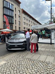 �koda Roadshow Bühne im Hintergrund; davor graues Skoda Fahrzeug mit mehreren interessierten Personen daneben.