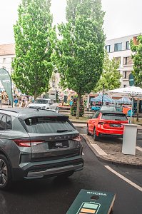Graues und rotes Skoda Fahrzeug, Bäume und Stände im Hintergrund.