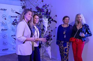 Vier Frauen, die in einem blau beleuchteten Raum einem Blumengesteck posieren.