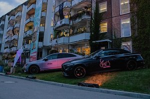 Zwei Mercedes-Benz Fahrzeuge, die nebeneinander auf einer beleuchteten Rasenfläche vor einer Wohnhausfassade präsentiert werden.