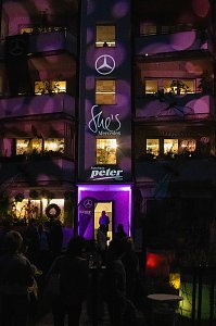 Eine Fassade, die lila beleuchtet ist und Logos von Mercedes, She�s Mercedes sowie der Autohaus Peter Gruppe trägt.