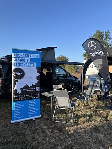Stand vom Autohaus Peter. Im Vordergrund ein großes blaues Werbebanner mit Firmeninfos. Dahinter eine V-Klasse Marco Polo mit geöffnetem Campingdach. Davor stehen ein Tisch und zwei Campingstühle. Rechts eine Mercedes-Fahne und ein Pavillon.