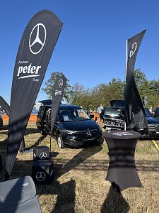 Stand vom Autohaus Peter. Im Vordergrund schwarze Mercedes-Fahnen, Sitzwürfel und ein Stehtisch. Dahinter parkt ein EQT. Rechts daneben steht der neue elektrische GLC.