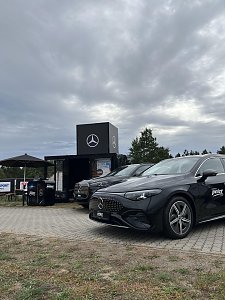 Zwei schwarze Mercedes-Benz Fahrzeuge stehen vor dem Promotion-Stand. Ein Stehtisch mit Sonnenschirm lädt Besucher zum Verweilen und Informieren ein.