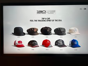Digitaler Bildschirm zeigt zehn historische und moderne Kopfbedeckungen in zwei Reihen. Oben steht das Logo 130 YEARS TRUCKS und die Aufforderung TAP A CAP. FEEL THE TRUCKING SPIRIT OF THE ERA.