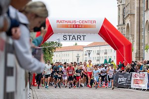 Man sieht viele L&auml;ufer und L&auml;uferinnen beim Start eines Laufs. Zuschauer fotografieren und im Hintergrund sieht man die Kulisse der Dessauer Innenstadt.