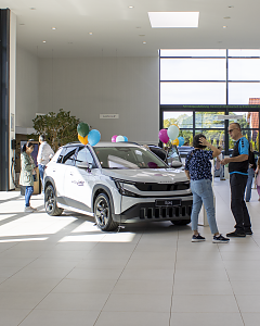 Ein wei&szlig;er �koda Epiq mit bunten Luftballons steht im Autohaus. Besucher informieren sich &uuml;ber das neue elektrische SUV.