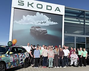 Gruppenfoto des Teams und der Beteiligten vor dem �koda-Autohaus mit farbenfroh foliertem Aktionsfahrzeug und gro&szlig;er �koda-Werbefl&auml;che.
