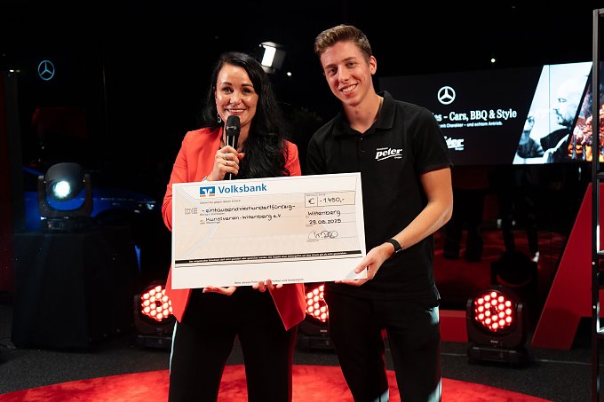 Christina Dost im roten Blazer und ein junger Mann im schwarzen Polohemd halten gemeinsam einen &uuml;bergro&szlig;en Spendenscheck mit dem Logo der Volksbank.